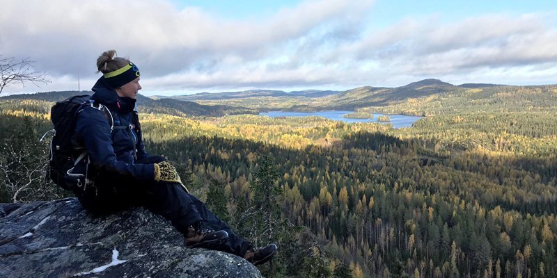 Vildmarksguiden Saana Lappalainen sitter med rinkan på ryggen på en hög klippa i Koli. Till höger öppnar sig ett skogslandskap.