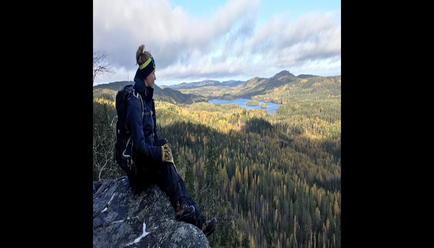 Vildmarksguiden Saana Lappalainen sitter med rinkan på ryggen på en hög klippa i Koli. Till höger öppnar sig ett skogslandskap.