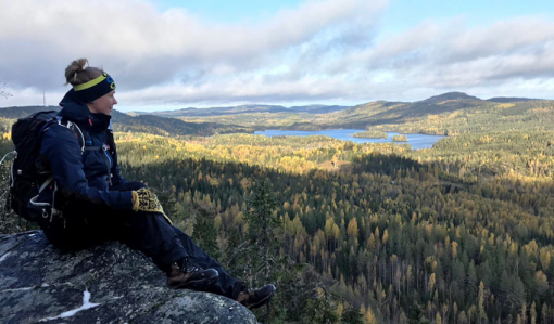 Vildmarksguiden Saana Lappalainen sitter med rinkan på ryggen på en hög klippa i Koli. Till höger öppnar sig ett skogslandskap.