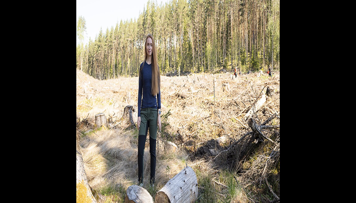 Inna Salminen står vid ett avverkat område. I bakgrunden syns två personer som planterar träd.