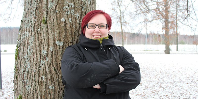 Hanna Parviainen står med armarna i kors intill ett träd ute på gården och tittar in i kameran. Det är ett tunt snötäcke på marken.