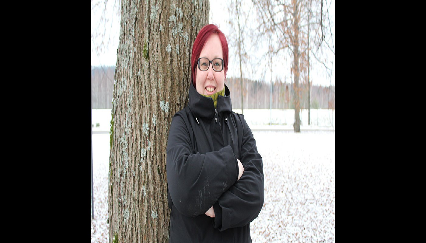 Hanna Parviainen står med armarna i kors intill ett träd ute på gården och tittar in i kameran. Det är ett tunt snötäcke på marken.