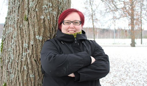 Hanna Parviainen står med armarna i kors intill ett träd ute på gården och tittar in i kameran. Det är ett tunt snötäcke på marken.