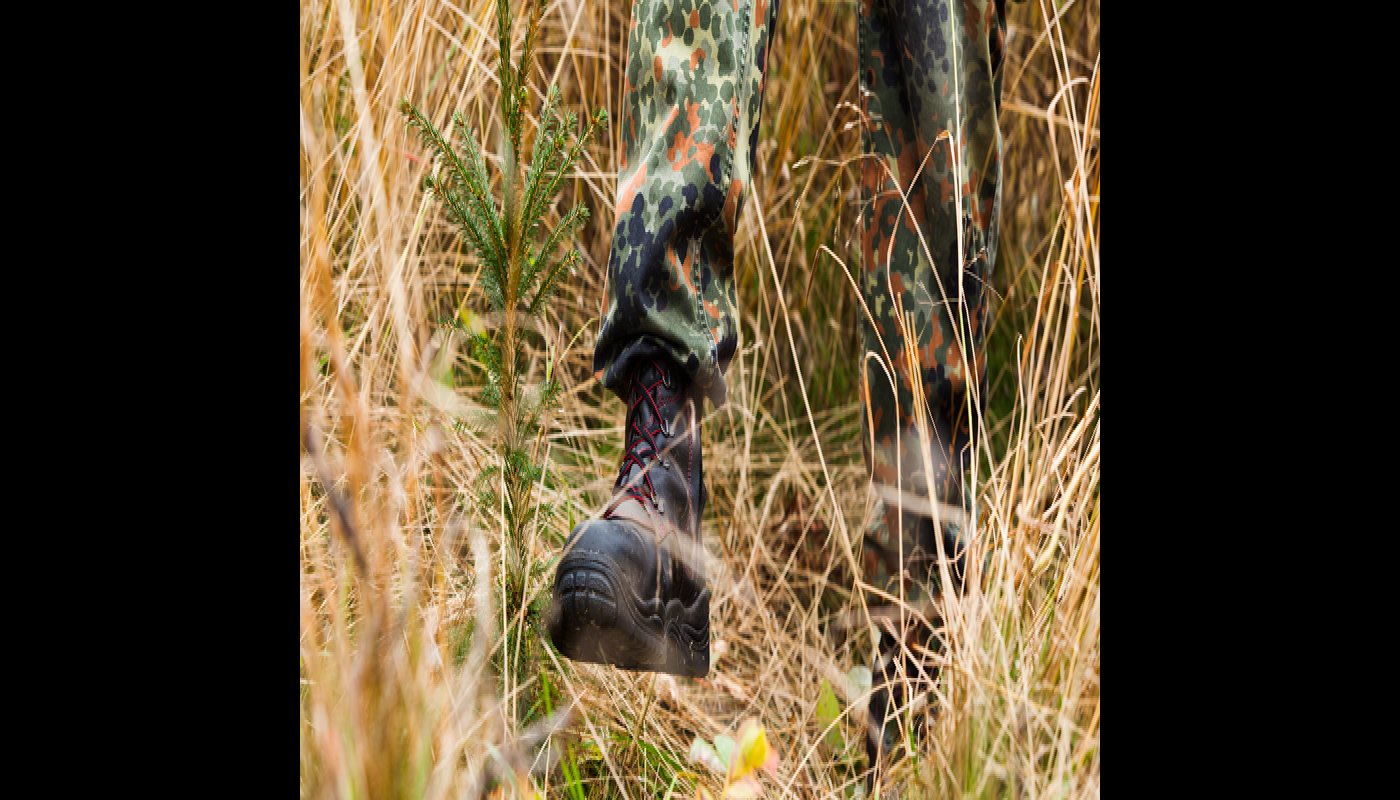 Närbild på de stadiga kängorna när en person trampar ner gräs runt en planta.