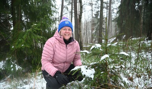 Heli Lehtomäki sitter på huk bredvid en liten gran. 