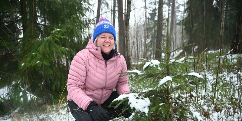 Heli Lehtomäki sitter på huk bredvid en liten gran. 