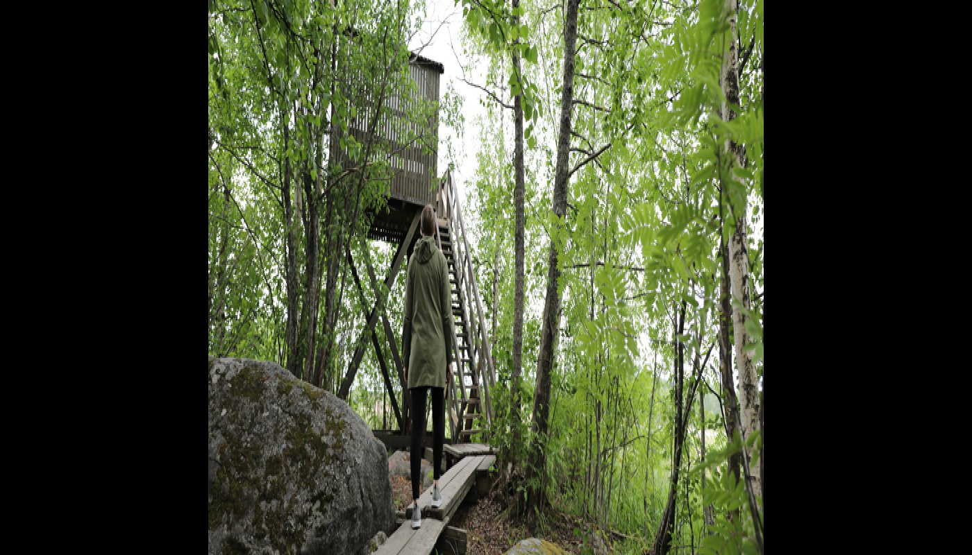 En person med ryggen vänd mot kameran går mot ett fågeltorn på sommaren.