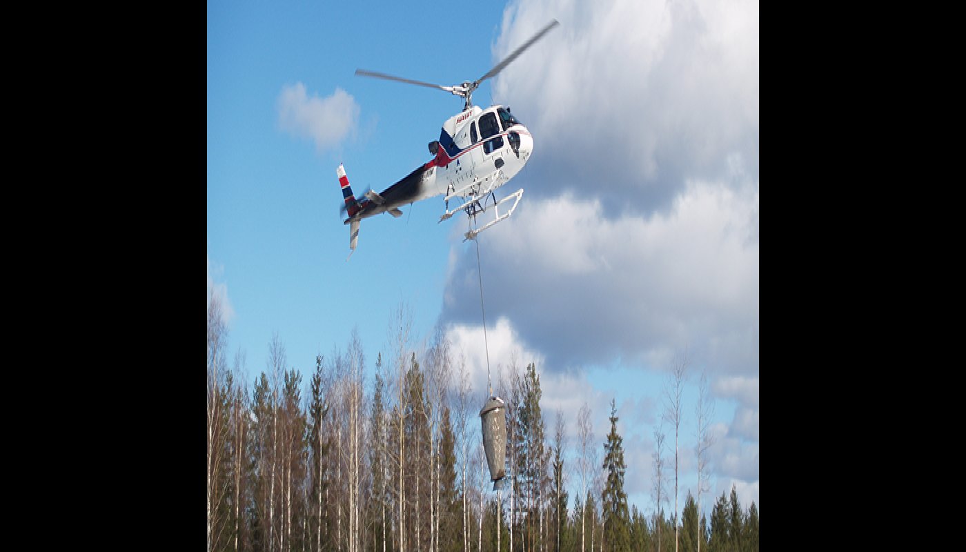Helikoptern sprider ut askgödselmedel i skogen. 