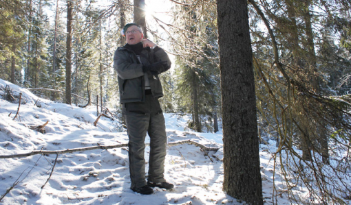 Timo Nissinen står i skogen som nu är skyddad permanent. Solen skiner bakom honom, och det är snö på marken.