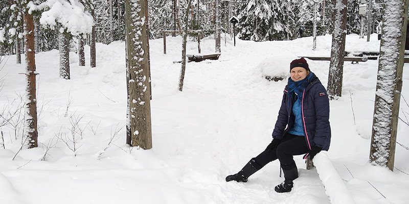 Anni Pylvänäinen sitter på en trädstam i en vintrig skog.