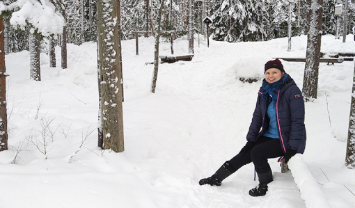 Anni Pylvänäinen sitter på en trädstam i en vintrig skog.
