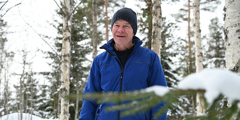 Tapani Isotalo står bland björkarna i skogen på vintern. Längre bort syns snöiga granar.