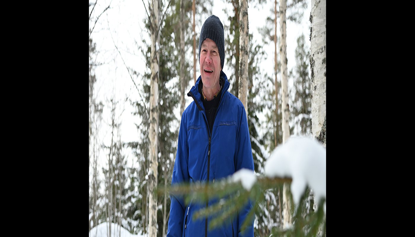 Tapani Isotalo står bland björkarna i skogen på vintern. Längre bort syns snöiga granar.