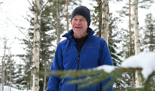 Tapani Isotalo står bland björkarna i skogen på vintern. Längre bort syns snöiga granar.