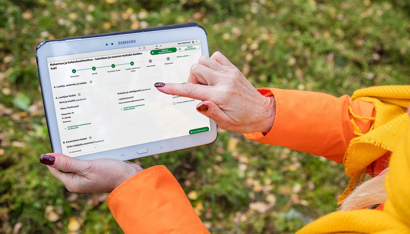 En person pekar med fingret på en surfplatta där tjänsten Metsään.fi är öppen.