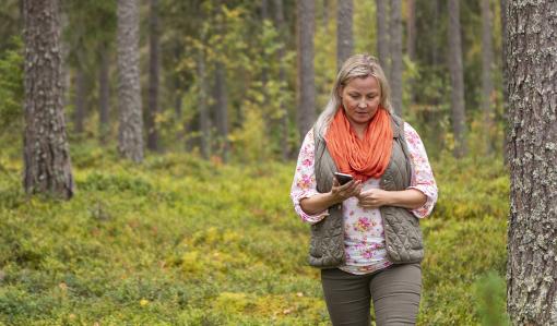 Kvinna går i skogen med en telefon. 
