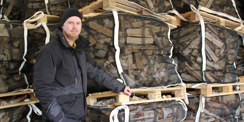 Esa-Pekka Penttilä står vid stora genomskinliga tygsäckar med ved.