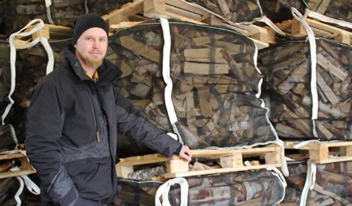 Esa-Pekka Penttilä står vid stora genomskinliga tygsäckar med ved.