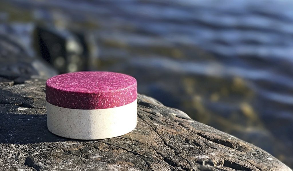 Sulapacs träbaserade förpackning utan mikroplast har fotograferats på en sten vid vattnet.