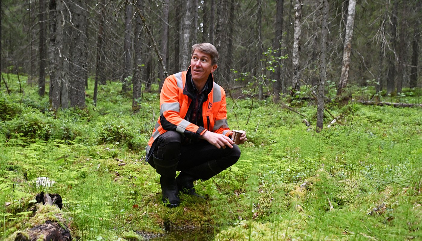 Jussi Vatanen sitter på huk intill en källa i skogen.