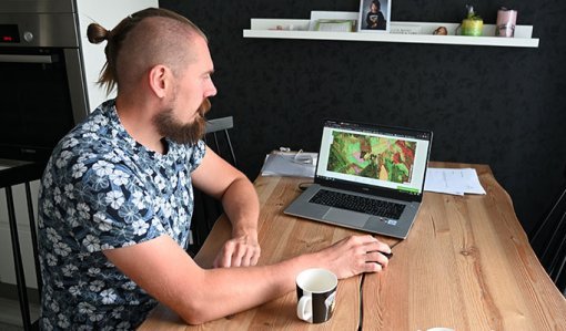 Tuomas Vakkila sitter vid köksbordet och tittar i tjänsten MinSkog.fi på en dator.