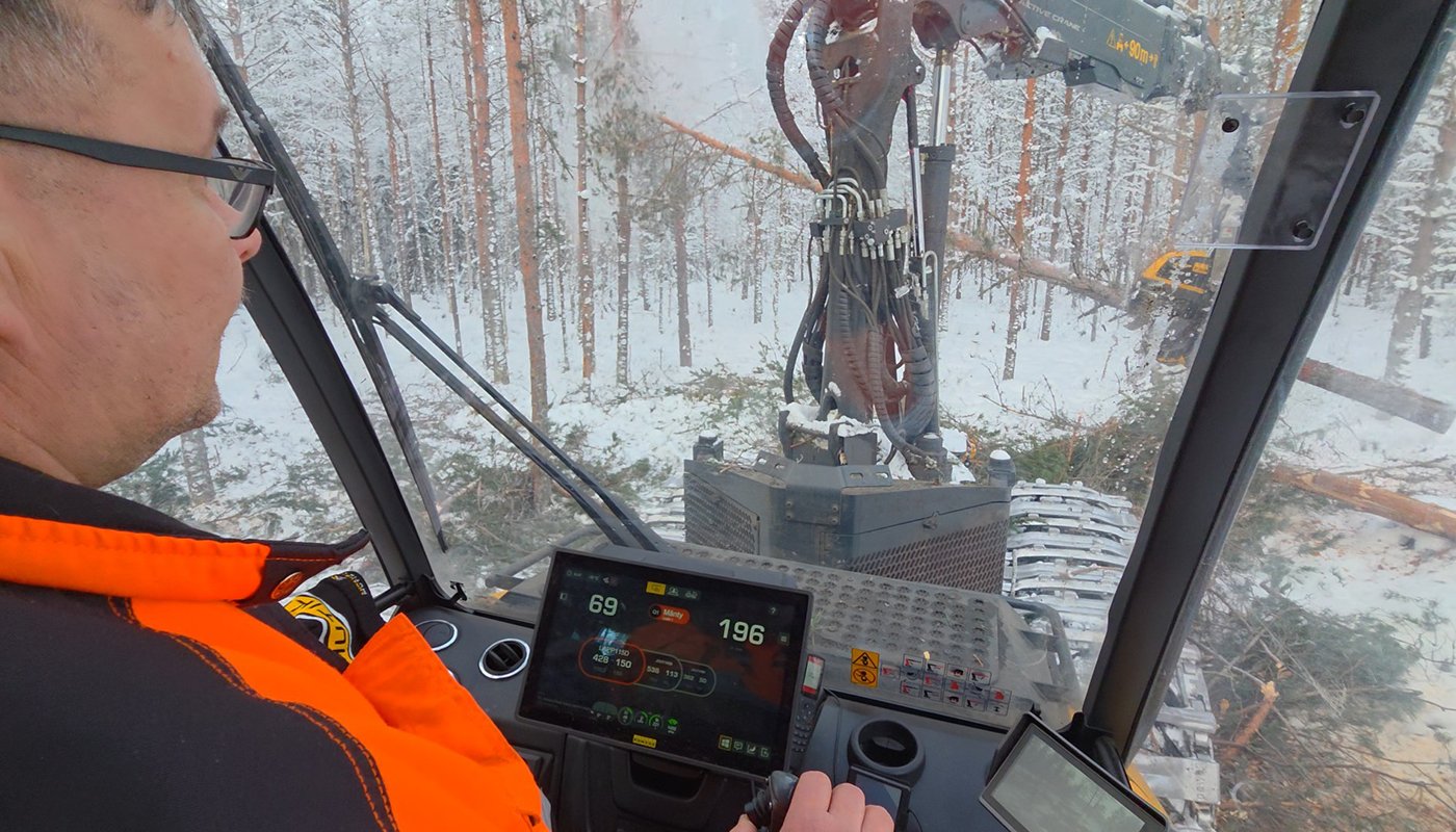 En bild på avverkningsmaskinens förarhytt. Maskinen fäller träd i vinterskogen.