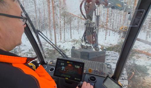 En bild på avverkningsmaskinens förarhytt. Maskinen fäller träd i vinterskogen.