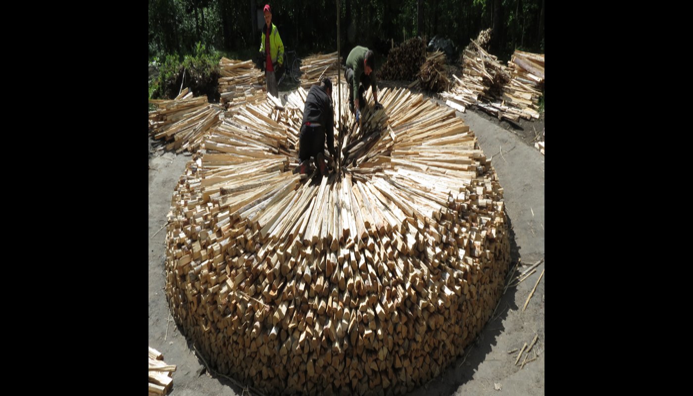 Två män travar ved i en rund konstruktion som ska bli en tjärdal. En annan man står bredvid och ser på.