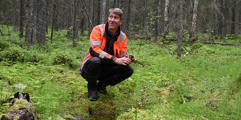 Jussi Vatanen sitter på huk intill en källa i skogen.