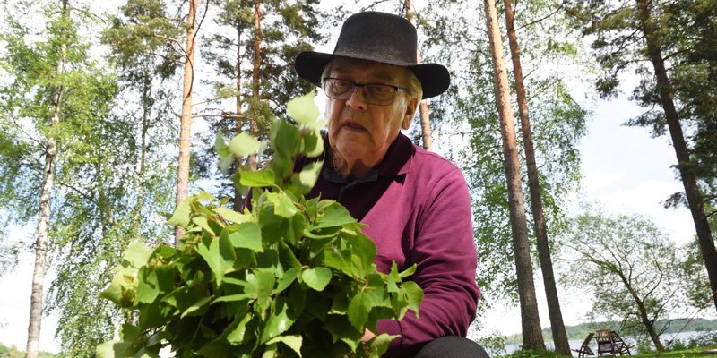 En man sitter utomhus och tillverkar en bastukvast av björkris.