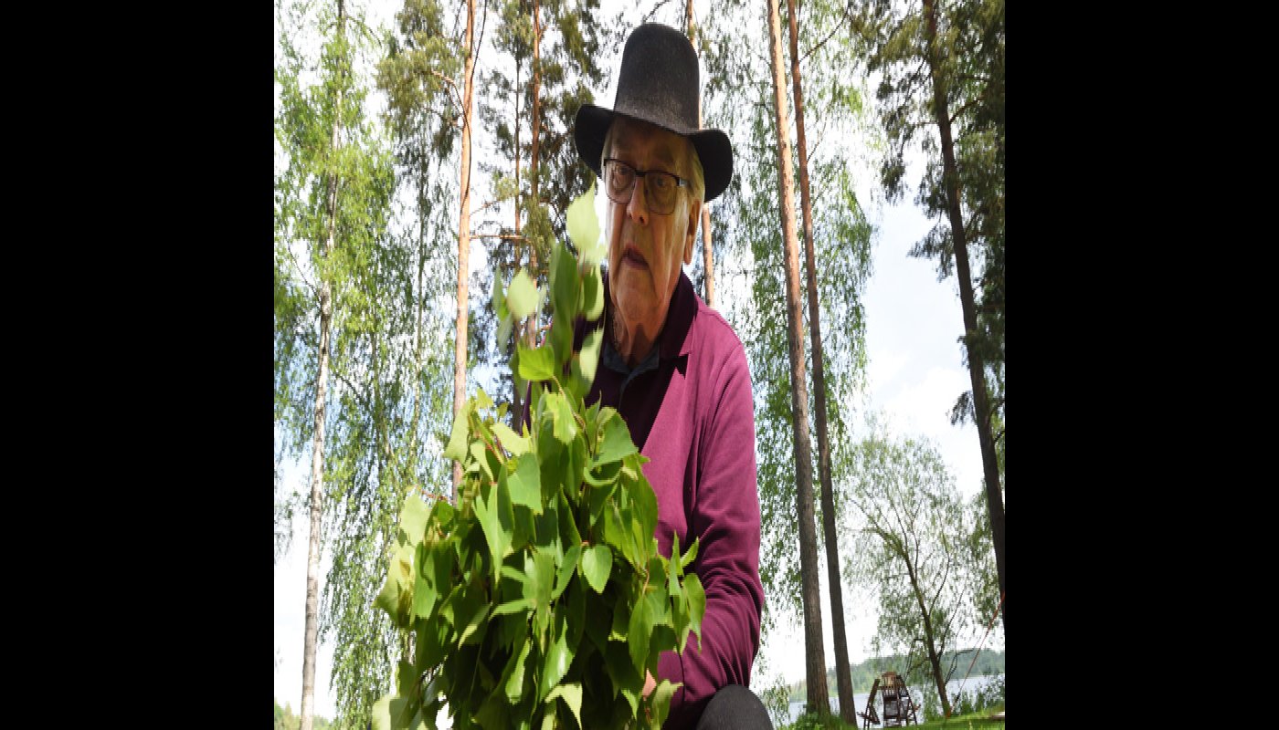 En man sitter utomhus och tillverkar en bastukvast av björkris.