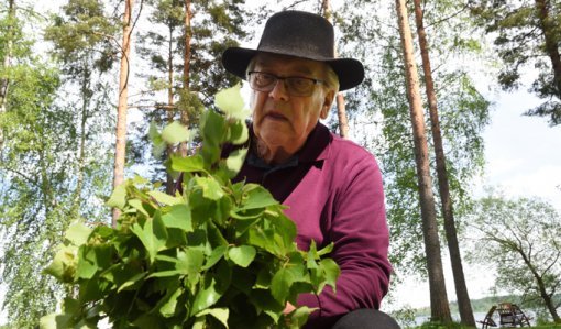 En man sitter utomhus och tillverkar en bastukvast av björkris.