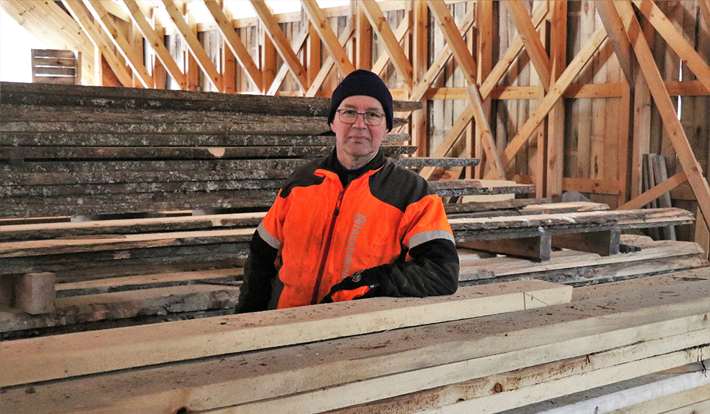 Jarmo Sirola står mellan två brädstaplar i en lagerbyggnad.