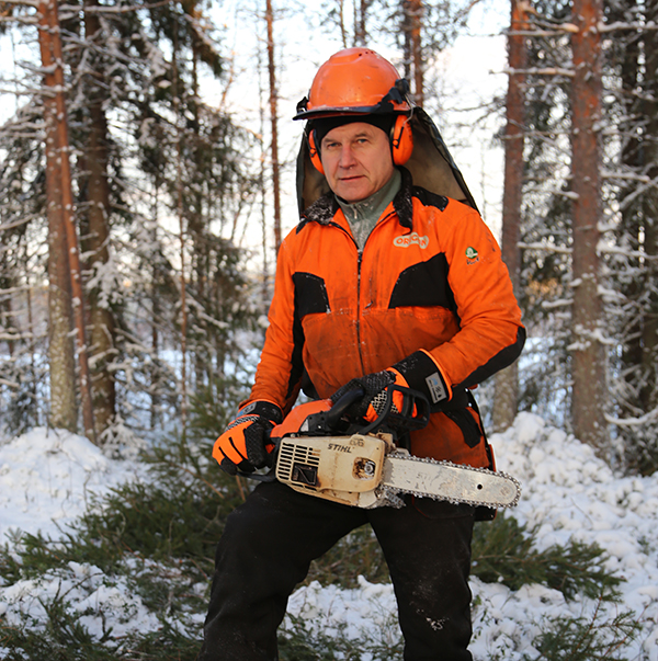 Alpo Särkelä i orange-svart skyddsmundering med motorsåg i en vintrig skog.