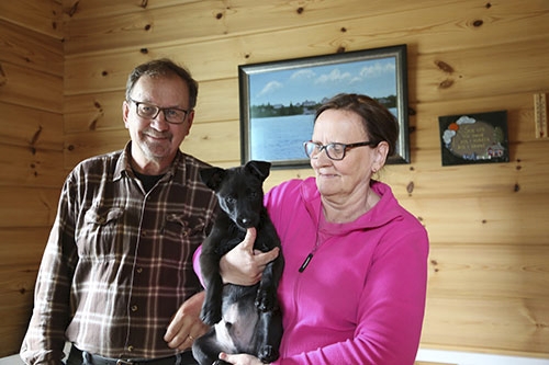 Reino Ronkainen och Hilkka Ronkainen som äger semesterstuga i timmer. I famnen håller Hilkka hunden Remy.