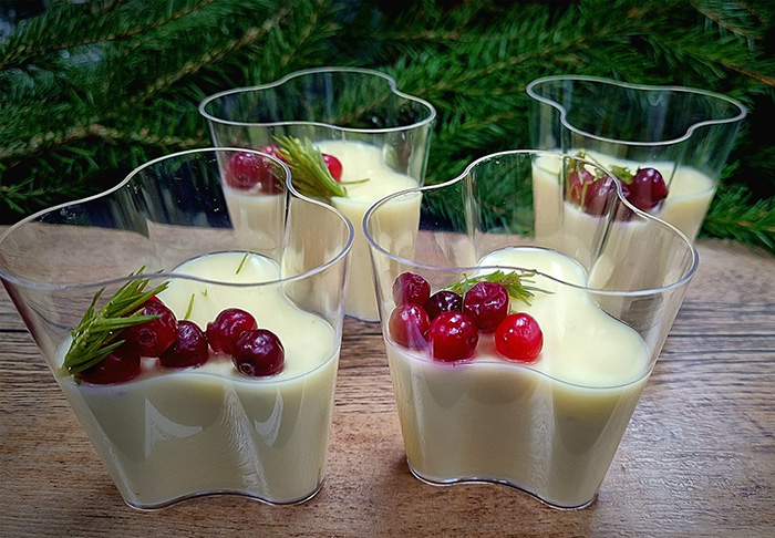I fyra glasskålar finns efterrätten granskottsposset. Ovanpå portionerna finns tranbär och granskott. I bakgrunden finns grankvistar som dekoration.