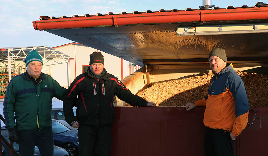 Mikko, Ville och Antti Palomäki står vid en container med träflis.