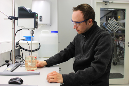 Laborant Karri Björklund blandar tillsatser i massan som består av träfiber. Han befinner sig i ett laboratorium och har skyddsglasögon på sig.