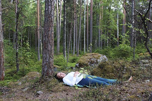 Elina Iivonen ligger på rygg under en tall med händerna på magen.