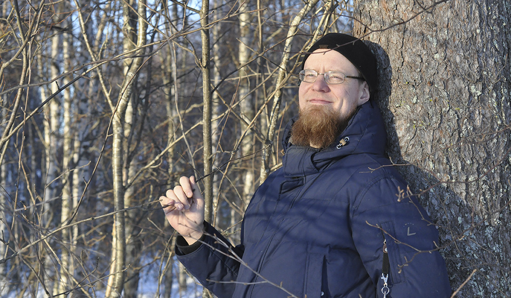 Juha Inkilä lutar mot ett träd i skogen.