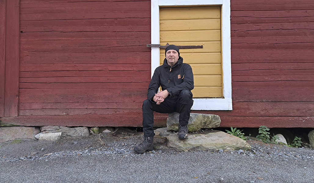 Marko Ämmälä sitter på stentrappan till en röd stockbyggnad.