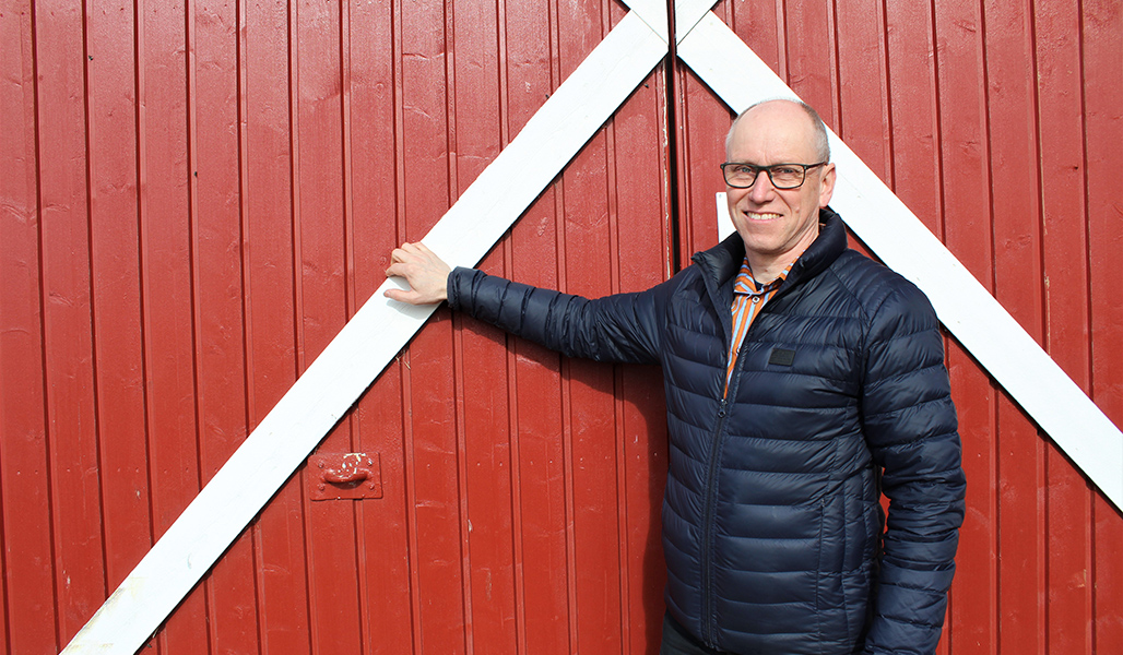 Martti Kangasniemi står vid en rödmålad trävägg.