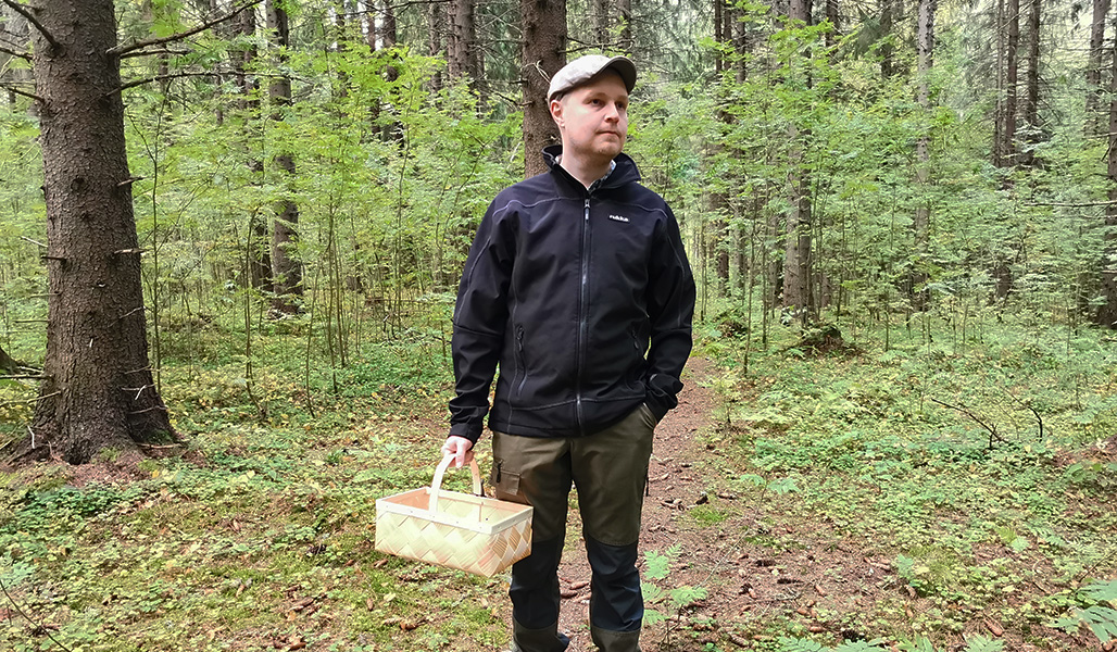 Jarno Kinnunen står i skogen med en svampkorg i handen.