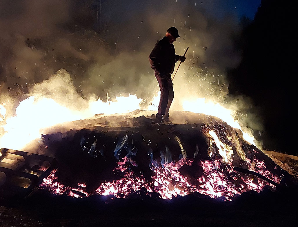 Tjärdalen brinner på natten och en man står uppe på den och vaktar medan den brinner.