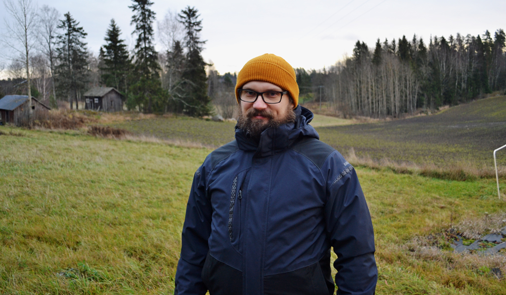 Torbjörn Granberg fotograferad med gamla lador och ett åkerlandskap i bakgrunden.